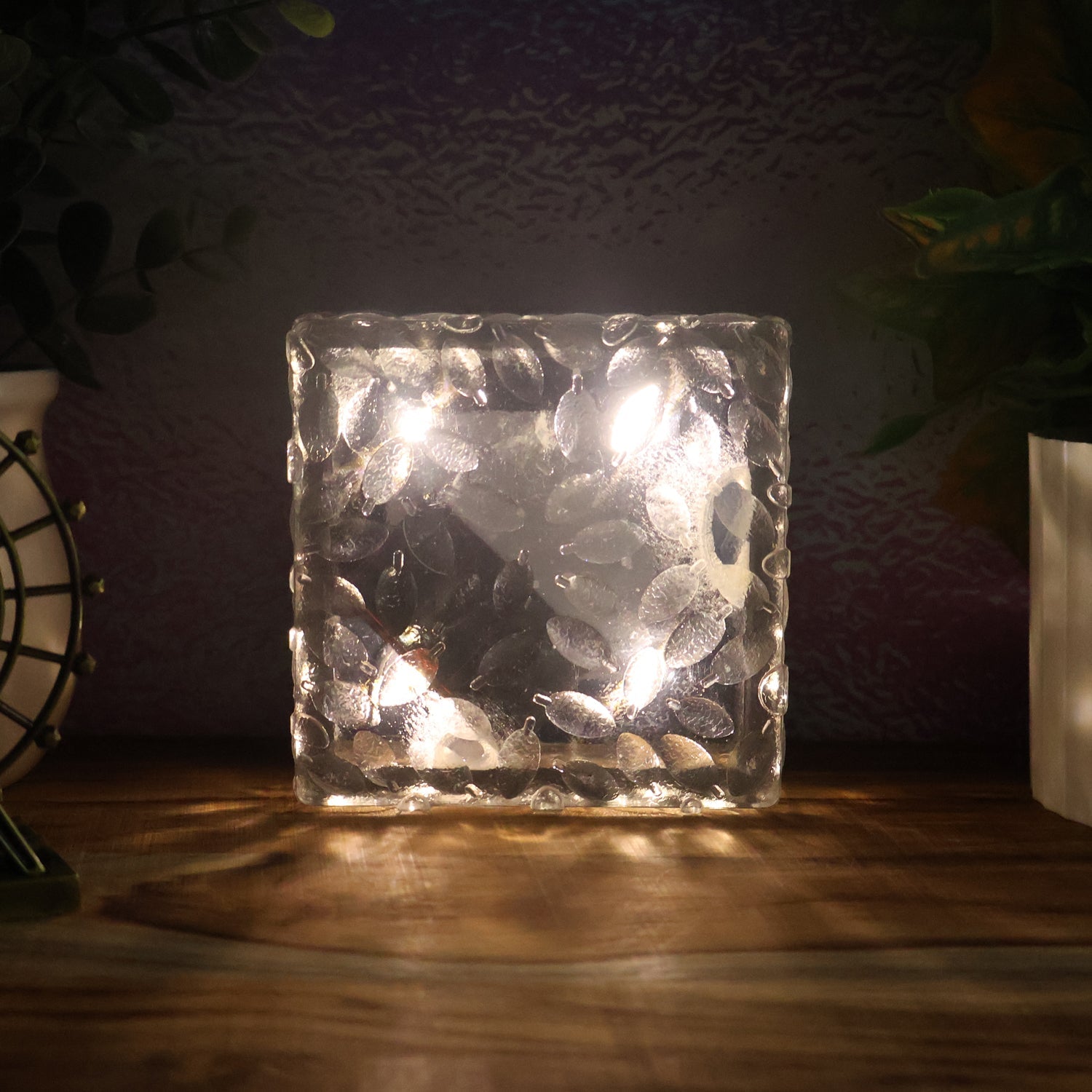 A single ice cube shaped solar garden light glowing warmly on a dark surface.