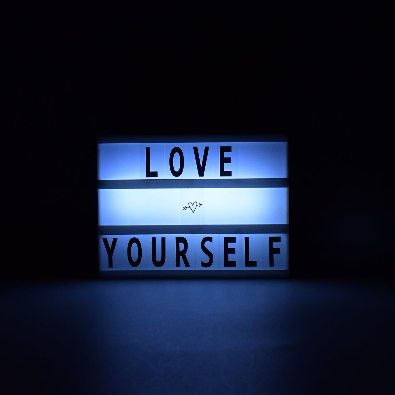 Black Mini A6 Cinematic Light Box displaying a custom message on a wooden surface.