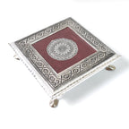 Close-up of the silver pooja chowki, highlighting an embossed peacock motif detail.